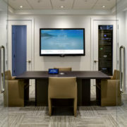 Open glass doors in front of a conference room featuring a display and center table with a Crestron touchpad.