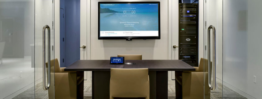 Open glass doors in front of a conference room featuring a display and center table with a Crestron touchpad.