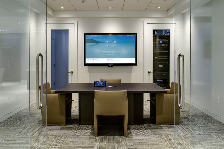 Open glass doors in front of a conference room featuring a display and center table with a Crestron touchpad.