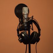 A close up of headphones hanging off a microphone in front of a black background.