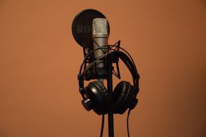 A close up of headphones hanging off a microphone in front of a black background.