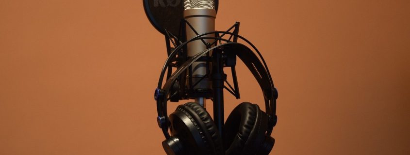 A close up of headphones hanging off a microphone in front of a black background.