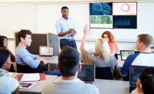 An educator takes questions from students in a corporate training room.