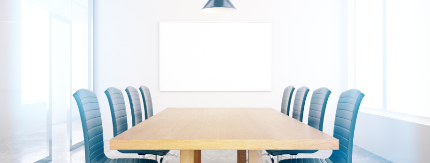 Well lit conference room with six blue chairs and a white board.