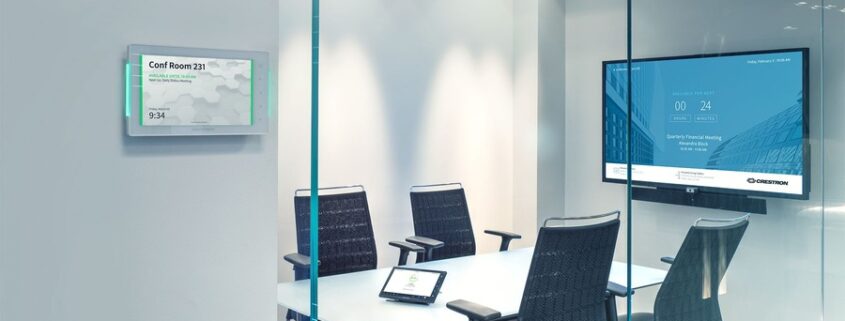 Photo of an empty huddle room, with four chairs placed around a table, a television on the wall, and a smart thermostat outside the room.