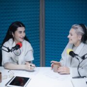 Two women in a foam-covered recording studio using podcast streaming solutions.