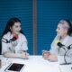 Two women in a foam-covered recording studio using podcast streaming solutions.