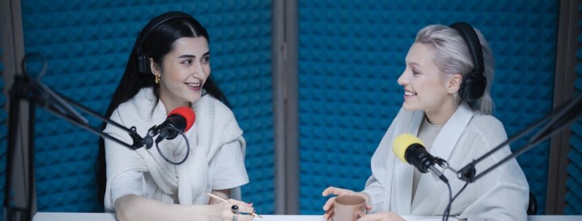 Two women in a foam-covered recording studio using podcast streaming solutions.