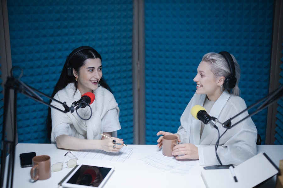 Two women in a foam-covered recording studio using podcast streaming solutions.
