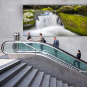 An escalator in front of a large LED video wall.