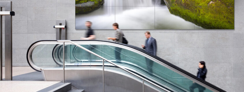 An escalator in front of a large LED video wall.