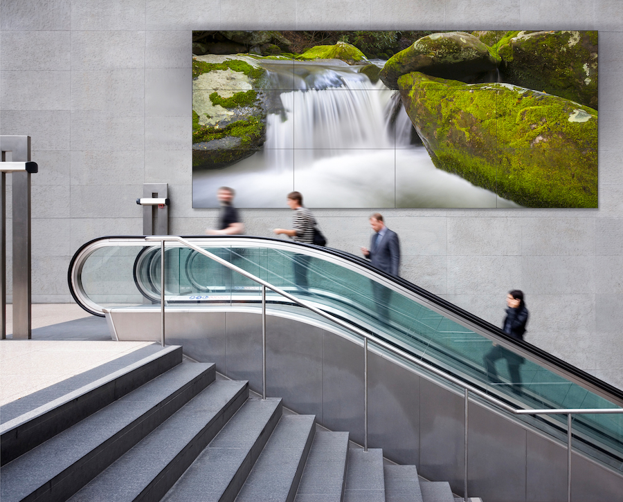 An escalator in front of a large LED video wall.