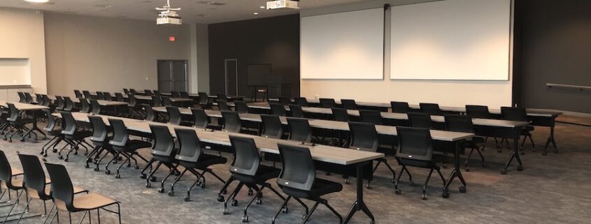 corporate training room with rows of tables, two projectors, and two projection screens