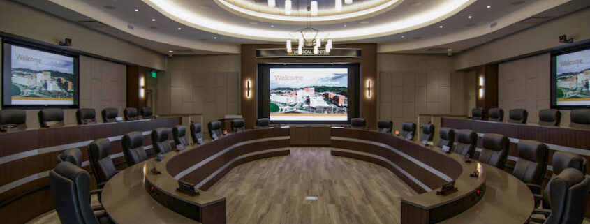 A large boardroom with many seats, a large screen, microphones, and speakers managed by remote monitoring services.