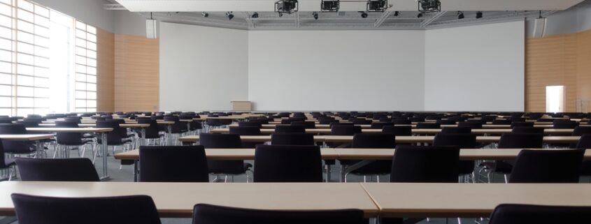 Large classroom with neatly arranged tables and chairs, equipped with overhead lighting and projection systems.