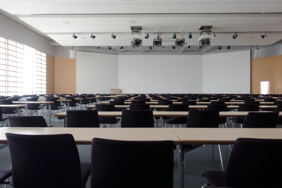 Large classroom with neatly arranged tables and chairs, equipped with overhead lighting and projection systems.