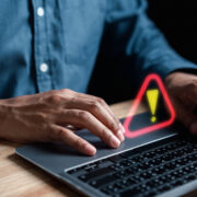 Person on a laptop with an exclamation mark floating above the keyboard.