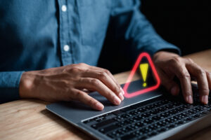 Person on a laptop with an exclamation mark floating above the keyboard.