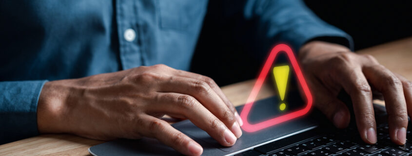 Person on a laptop with an exclamation mark floating above the keyboard.