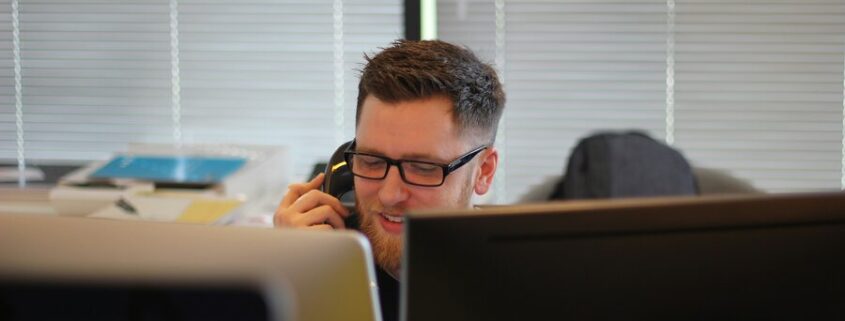 A man providing support services on the phone sitting in front of a computer.