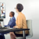 Crestron conference room software displaying video conferencing speakers on a wall-mounted TV in front of meeting table.