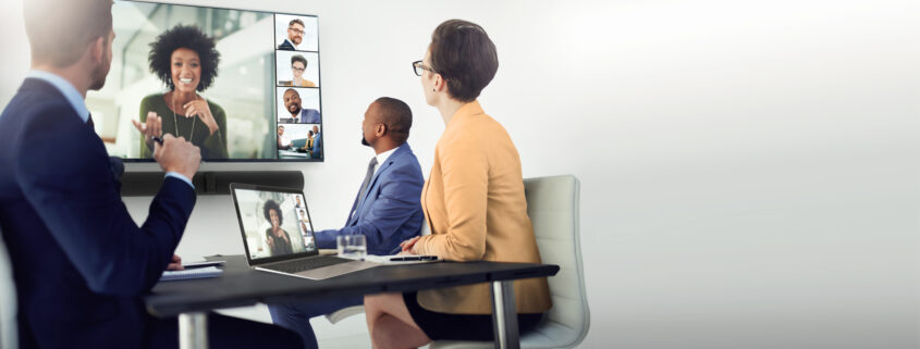 Crestron conference room software displaying video conferencing speakers on a wall-mounted TV in front of meeting table.