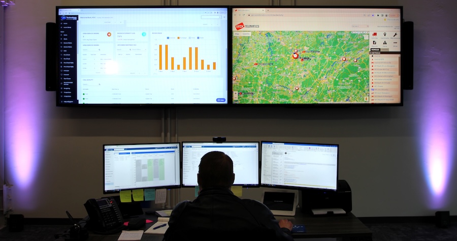 Operator monitoring AV system dashboards and live mapping across five displays in a commercial network operations center.