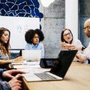 Staff members sit around a huddle space table. A Crestron tabletop control sits on the table.
