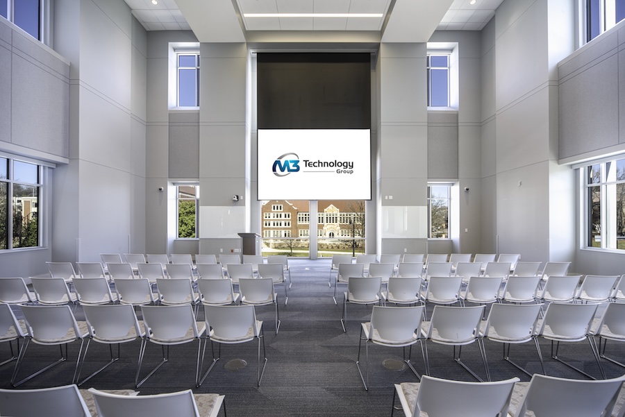Auditorium-style event space with rows of chairs and a large projection screen displaying the M3 Technology Group logo.