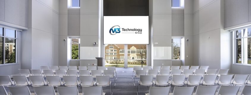 Auditorium-style event space with rows of chairs and a large projection screen displaying the M3 Technology Group logo.