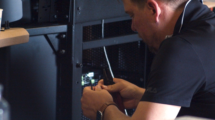 Worker kneels before an AV rack to examine wiring.
