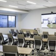 Hybrid training room with rows of ergonomic chairs, a large digital display, and integrated AV for collaboration.