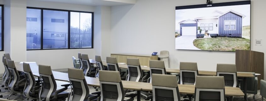 Hybrid training room with rows of ergonomic chairs, a large digital display, and integrated AV for collaboration.