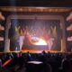 Live event stage with colorful red and yellow lights, theater seating in rows and balconies.