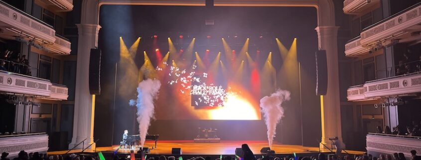 Live event stage with colorful red and yellow lights, theater seating in rows and balconies.