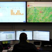 NOC operator monitoring real-time dashboards and telematics maps on a large video wall in a control room.