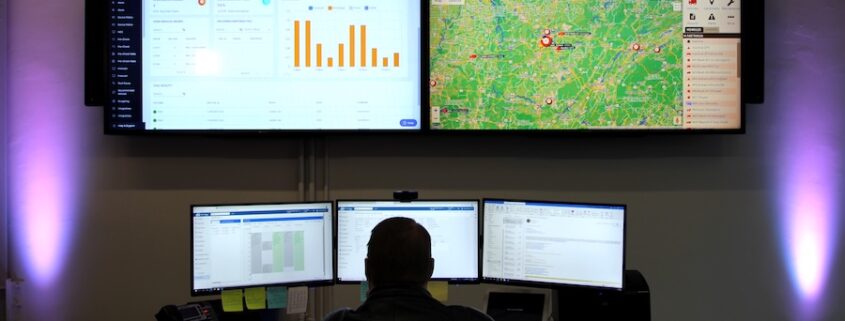 NOC operator monitoring real-time dashboards and telematics maps on a large video wall in a control room.