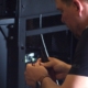 Technician using wire strippers to prep cable near an open AV equipment rack with exposed wiring and hardware.