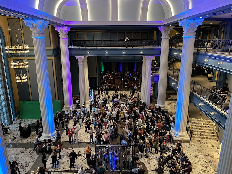 three-story live event space filled with event attendees. Lights are blue-hued and large columns frame the space.